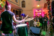 Ein Schlagzeuger spielt vor einem bunten Publikum in einem festlich beleuchteten Innenhof.