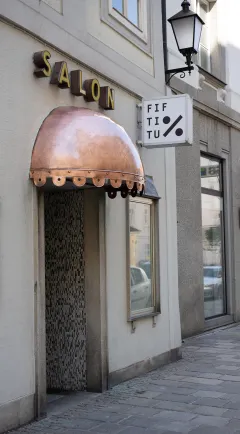Salon mit kupferner Markise, Straßenszene und Schaufenster rechts.