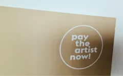 Beiges Plakat mit dem Text "pay the artist now!" in einem weißen Kreis.