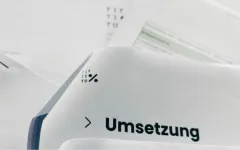 Dokument mit dem Wort "Umsetzung" und einem Logo, verschwommene Hintergrundtexte.