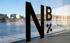 Logo „N×B“ auf Glaswand mit Fluss und Stadt im Hintergrund.