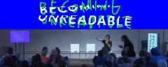 Bühne mit Vortrag, blauer Hintergrund, Publikum, Schriftzug "Becoming Unreadable".
