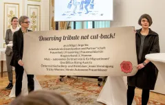 Zwei Personen halten ein Plakat mit Organisationen in einem festlichen Raum.