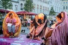 Menschen diskutieren lebhaft auf einer bunt dekorierten Bühne im Freien.