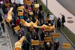 Demonstration mit gelben Bannern, Plakaten und bunter Kleidung auf einer Straße.