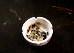 Weißer Aschenbecher mit Zigarettenstummeln und Asche.
