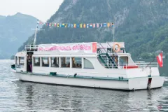 Weißes Boot auf einem See mit Bergen im Hintergrund.