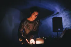 DJ in dunklem Raum mit blauer Beleuchtung, fokussiert auf Mischpult.
