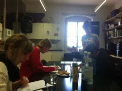 Personen sitzen in einem Raum am Tisch, schreiben. Lehrer stehend.