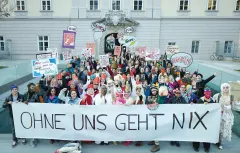 Große Gruppe Menschen mit Schildern und einem Transparent vor einem Gebäude.