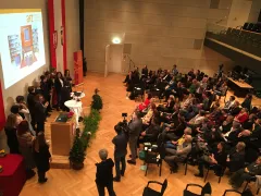 Mehrere Personen auf einer Bühne vor Publikum in einem Veranstaltungsraum.