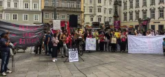 Protestierende Menschenmenge mit Bannern auf einem Stadtplatz.