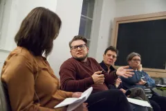 Gruppe von vier Personen diskutiert im Raum, Mann in rotem Pullover spricht.