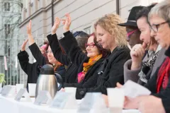 Personen bei einer Abstimmung, einige heben die Hand. Sie sitzen an einem Tisch im Freien.