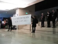Personen mit Transparent in modernem Gebäude, Publikum im Hintergrund.