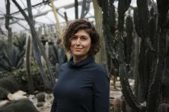 Frau steht lächelnd in einem botanischen Garten mit Kakteen.