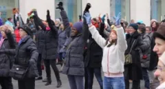 Menschen tanzen draußen, heben die Arme, bekleidet in Winterkleidung.