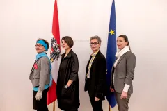 Vier Frauen in Business-Outfits, stehend vor österreichischer und EU-Flagge.