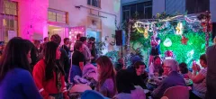 Feiernde Menschen bei bunter Beleuchtung in einem Innenhof mit Pflanzenwand.