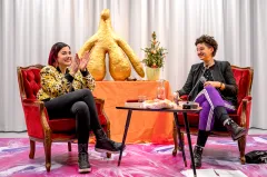 Zwei Frauen auf roten Sesseln, dazwischen ein Tisch und eine große goldene Skulptur.