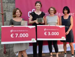 Vier Frauen posieren mit Preischecks und Trophäen vor einem rosa Banner.