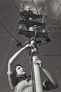 Frau klettert auf Strommast und überprüft Leitungen. Schwarz-weiß Fotografie.