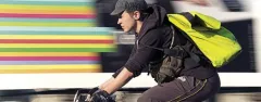 Radfahrer mit gelbem Rucksack, bunte Streifen im Hintergrund.