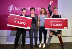 Vier Personen lächeln, halten große Schecks über 5.000 €, vor einem roten Banner.