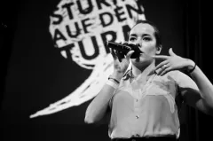 Schwarz-Weiß-Foto einer Frau mit Mikrofon auf der Bühne.