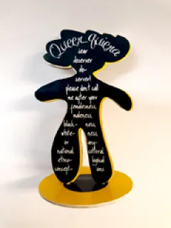 Schwarze Skulptur mit weißen Schriftzügen auf gelbem Sockel.